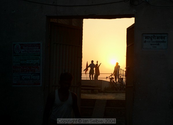 Sunrise over the Ganges, Varanasi.    People performing their morning exercises on the roof of a building are visible through a doorway in the wall