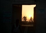 Sunrise over the Ganges, Varanasi.    People performing their morning exercises on the roof of a building are visible through a doorway in the wall