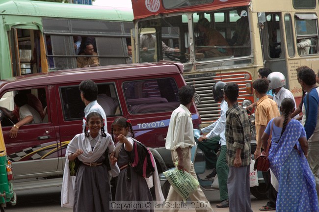 The girls are interested in the photographer while everyone else is watching two bus drivers fighting in the cab of one of them