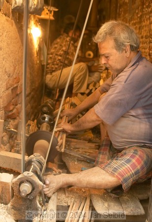Man cutting dowels to make curtain rings in a tiny factory, Old Delhi
