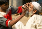 Young boy shaving the moustache of an old bearded man on the footpath by the street, Old Delhi