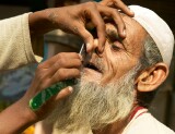 Young boy shaving the moustache of an old bearded man on the footpath by the street, Old Delhi