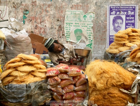 Man asleep behind his goods in the street market near the Tomb of Nizammudin, Delhi