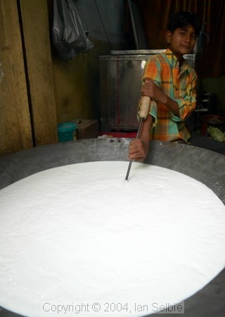 Boy stirring huge wok full of milk at the street market near the Tomb of Nizammudin, Delhi