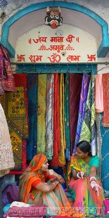 Two sales ladies chatting among their wares at the Janpath Lane textiles market, Delhi