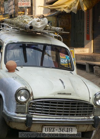 A corpse arrives at Harishchandra Ghat tied on top of an Ambassador car