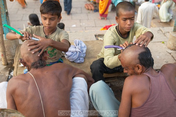 Shaving the heads of children and adults is a symbol of purification before bathing in the Ganges.   Here the children are shaving the elders