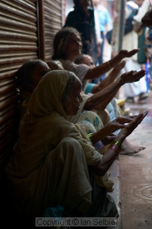 Beggars reach out for alms in a dark alley in old Varanasi